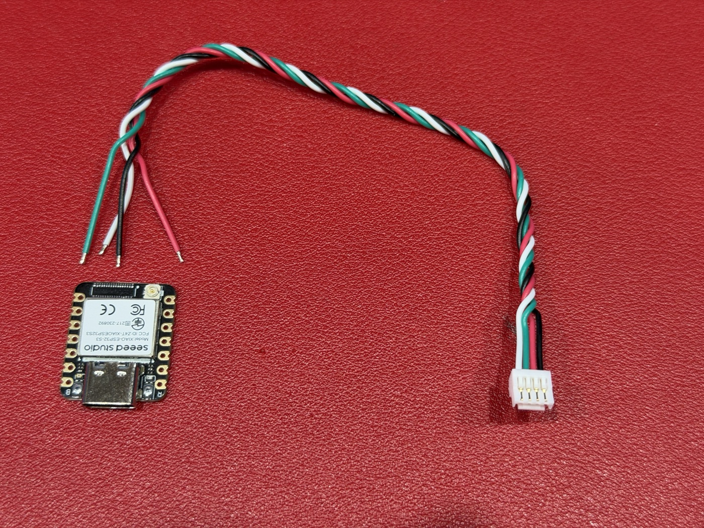 A Seeed XIAO ESP32-S3 beside the Nexus four-way lead, its plug on one end and four bare wires on the other: white, green, red and black